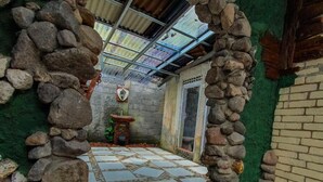 A stone archway leading to a tiled patio area with a rustic, green interior and a metal roof. - Aurora Living Merapi Jogja (Pakem)