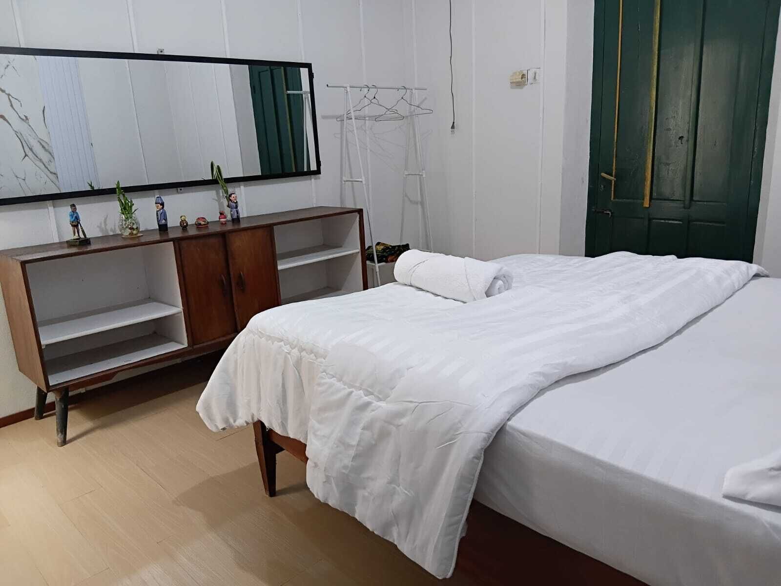 A bedroom with a bed, a wooden wardrobe, a mirror, and a green door.