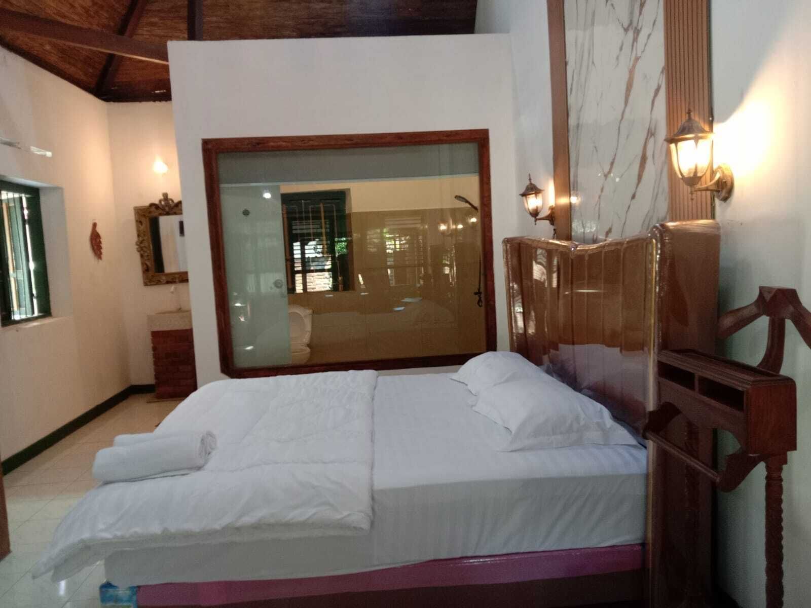 Un dormitorio con un espejo grande, una cama con ropa blanca, un cabecero de madera y una mesita de noche.