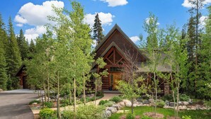 A log cabin with a stone foundation, surrounded by a landscaped garden with various plants and trees.