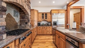 A kitchen with wooden cabinets, a stone fireplace, a stainless steel refrigerator, and a wooden countertop.