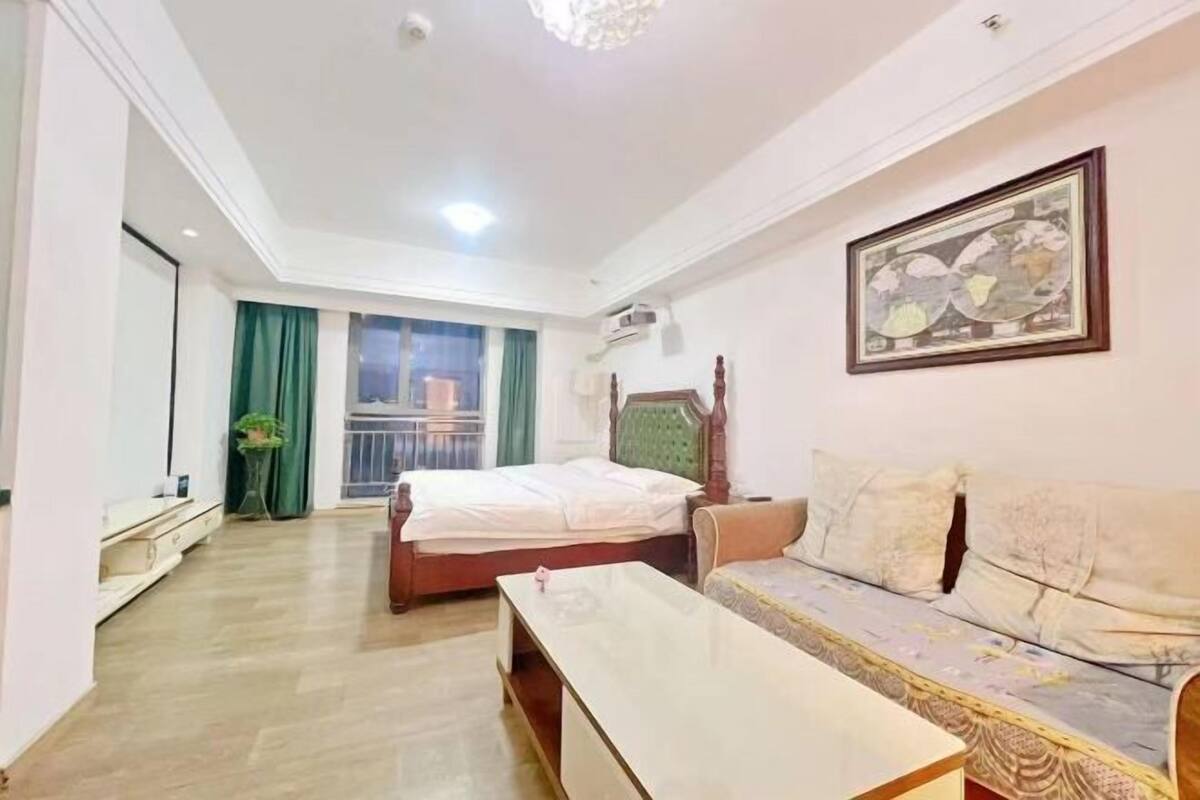 Une chambre d’hôtel avec un lit, un canapé, une petite table, une plante en pot et une fenêtre avec des rideaux.
