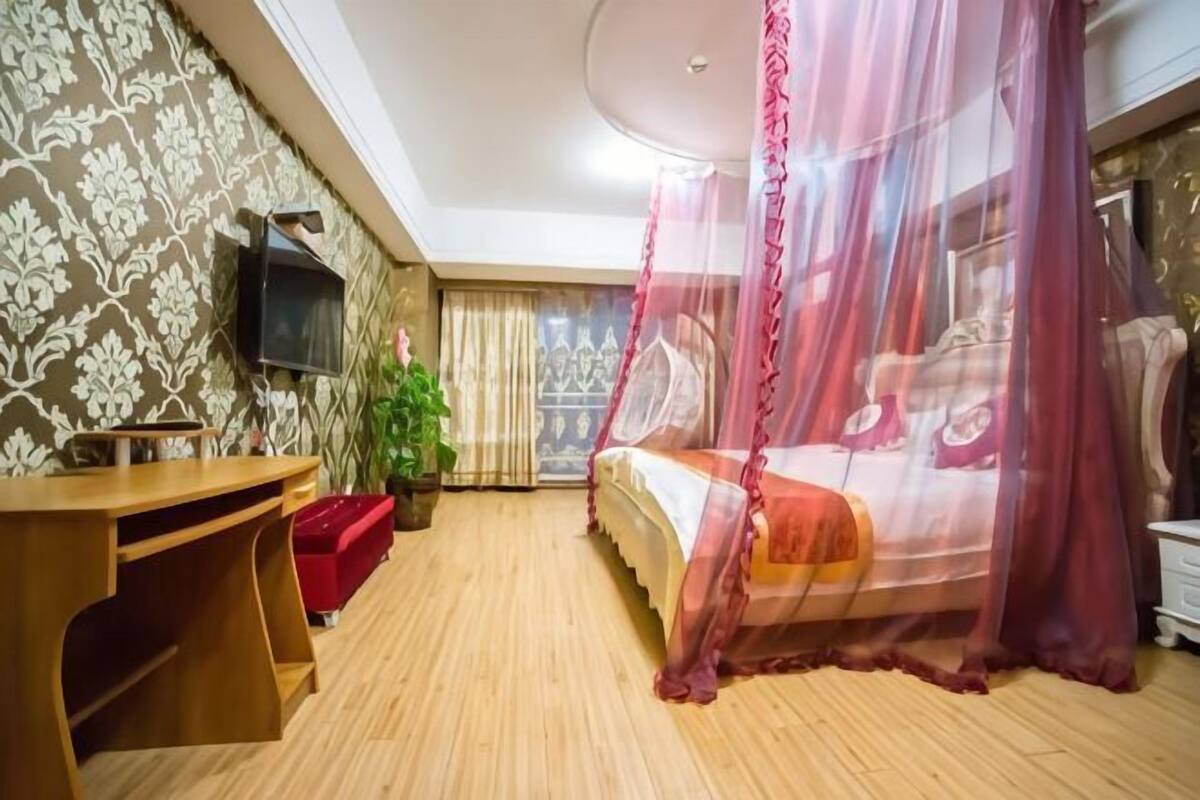 Une chambre à coucher avec un lit, un bureau, une télévision et une plante en pot.