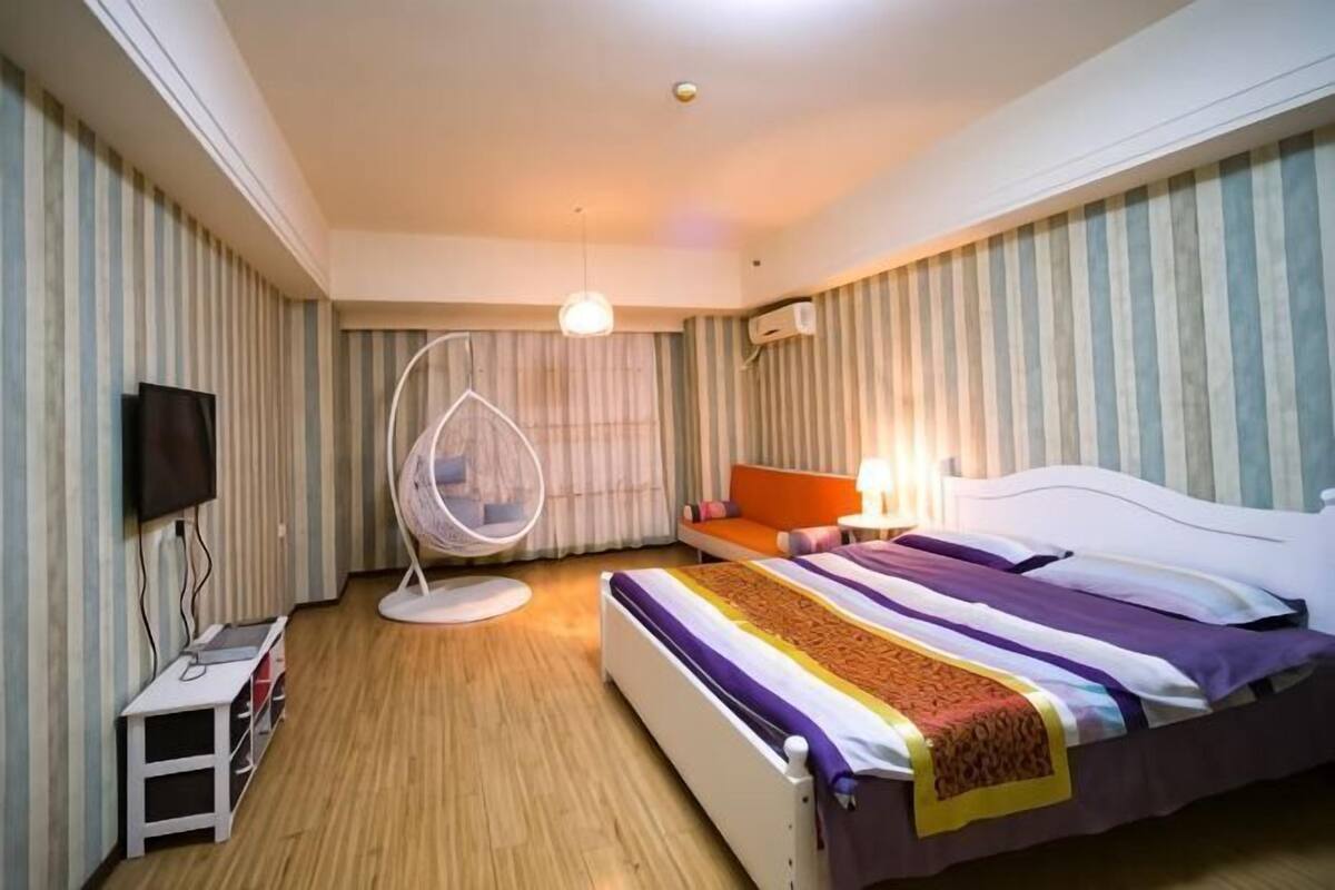 Une chambre d’hôtel avec un lit, une télévision, un fauteuil suspendu et une petite table.