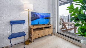 A room with a wooden TV stand, a blue chair, and a large window with a view of a wooden deck and mountains. - Mt Adams Studio+Steps to Art Museum+Fully Equipped+Stellar City Views+Fast Wifi (Cincinnati)