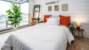 A modern bedroom with a large bed, a desk, and a chair. There is a window with a view of buildings outside. - Mt Adams Studio+Steps to Art Museum+Fully Equipped+Stellar City Views+Fast Wifi (Cincinnati)