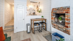 A compact kitchen with a white door, a small table with stools, a brick fireplace, and a microwave above the counter. - Mt Adams Studio+Steps to Art Museum+Fully Equipped+Stellar City Views+Fast Wifi (Cincinnati)