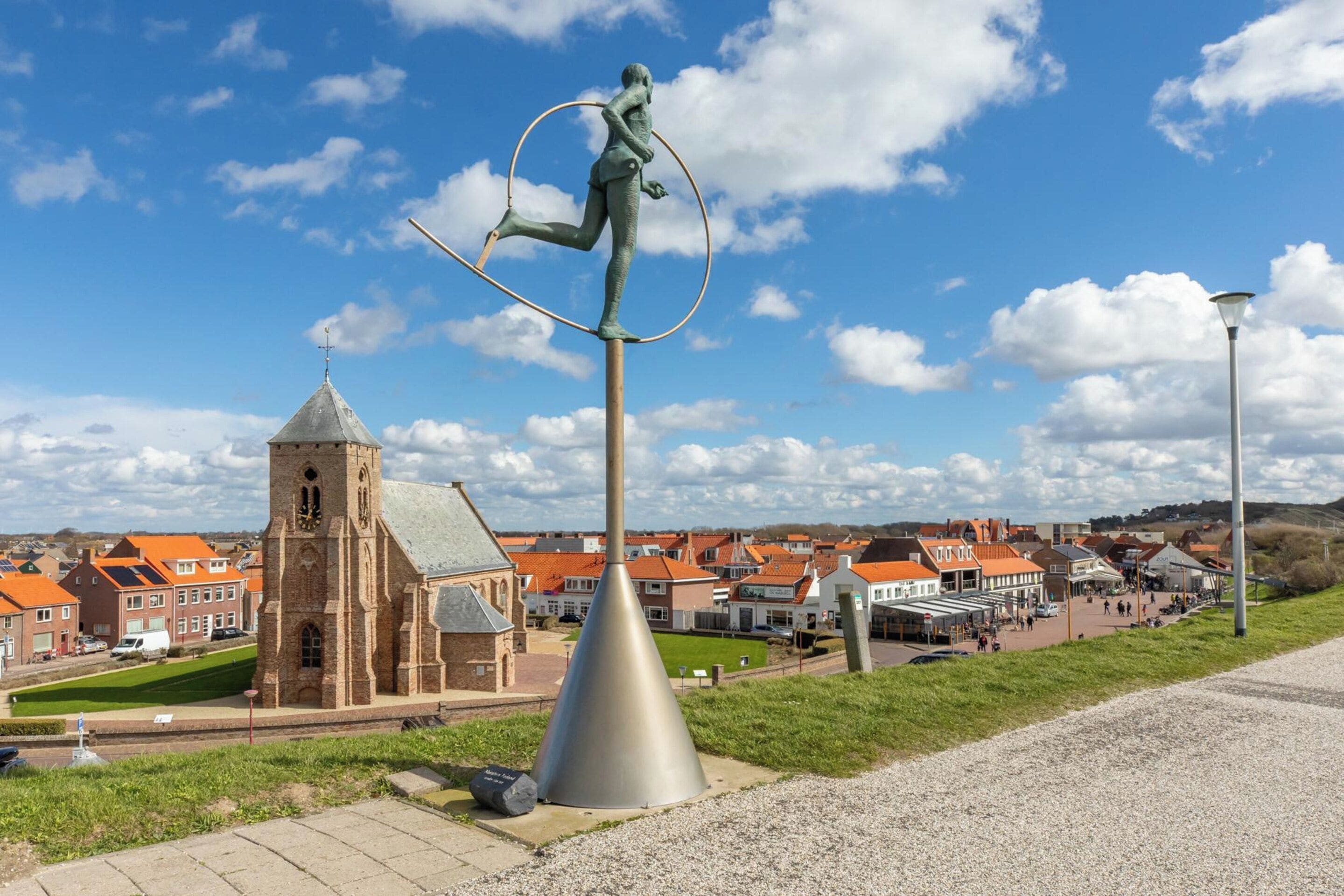 A sculpture of a figure balancing on a pole with a town in the background.