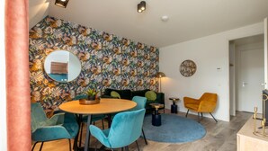 A modern living room with a round wooden table, teal chairs, a dark green sofa, and a vibrant floral wallpaper. - Wifi and Golden Beaches; Home (Zoutelande)