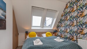 A bedroom with a large bed, two yellow pillows, a green quilted bedspread, and a window with blinds. - Wifi and Golden Beaches; Home (Zoutelande)