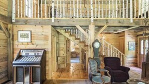 A wooden cabin interior with a staircase leading to a loft, a vintage keyboard, and two upholstered chairs.