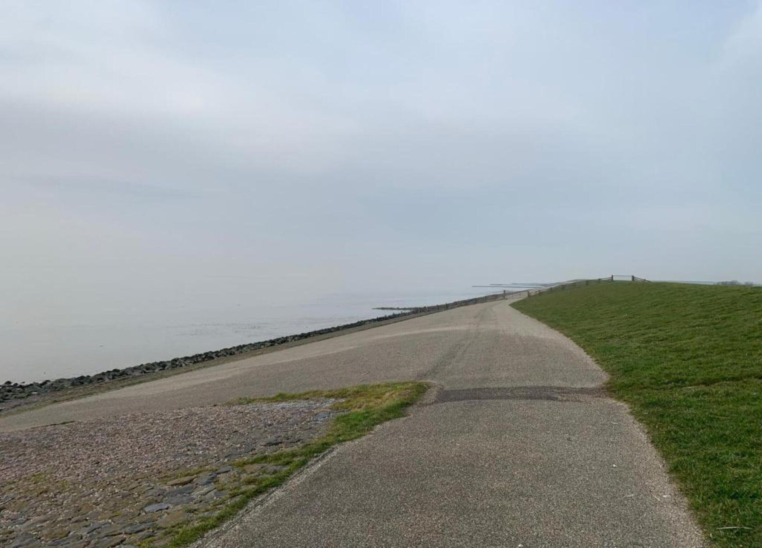 A gravel path alongside a body of water with a grassy area on the right.