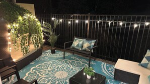 Un patio al aire libre con piso estampado, mobiliario de mimbre e iluminación con luces colgantes.