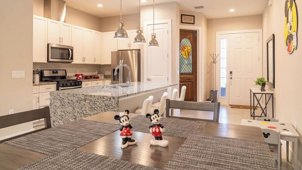 Una cocina moderna con armarios blancos, electrodomésticos de acero inoxidable y una encimera de granito. Hay dos figuras de Mickey Mouse sobre la mesa de comedor.