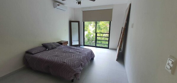 Un dormitorio con una cama, una mesita de noche, un espejo y un ventanal grande.