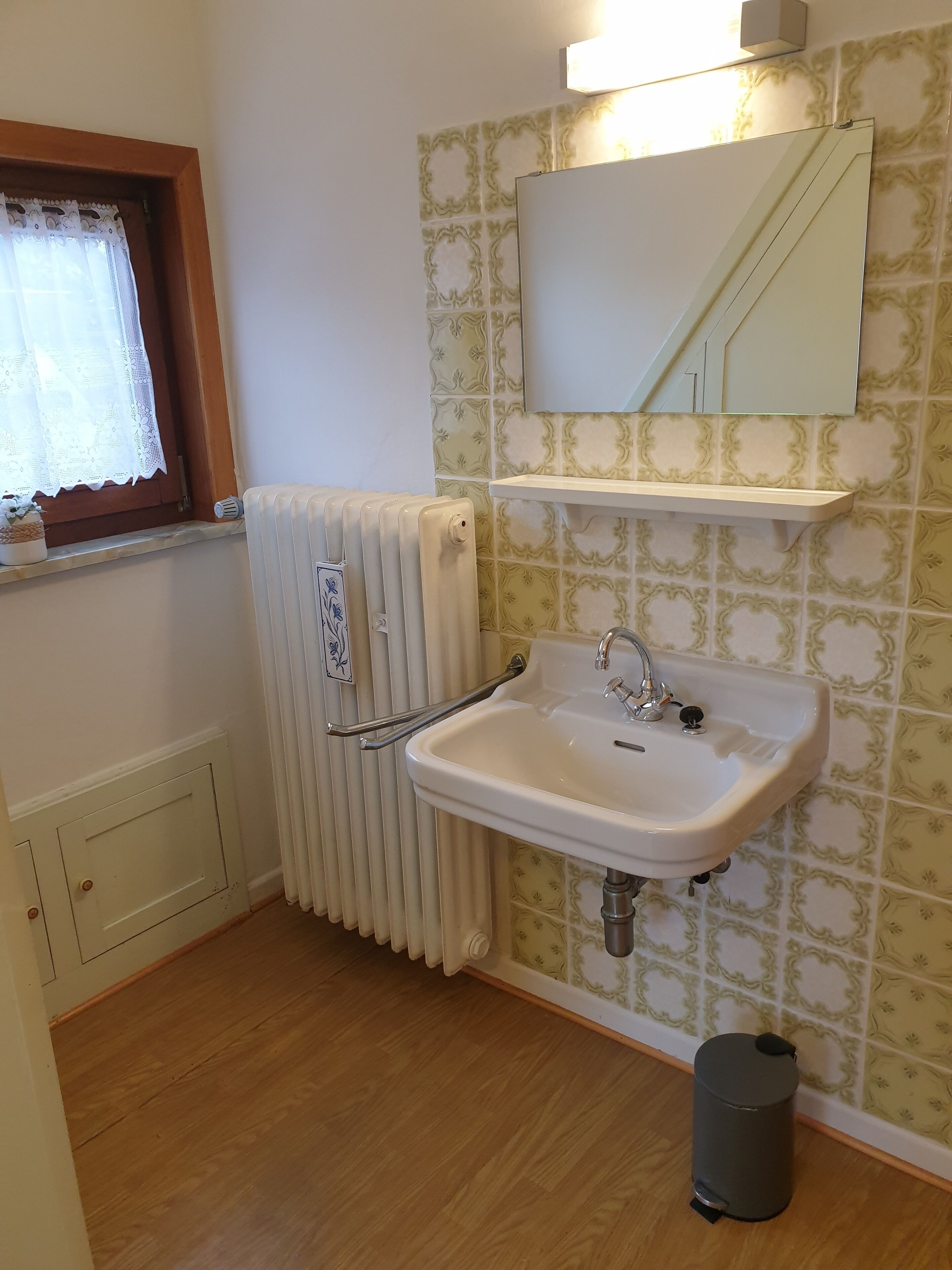 A bathroom with a white sink, a radiator, a mirror, and a trash bin.