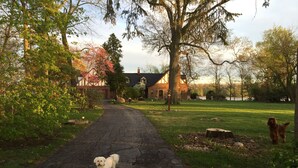 A rural road with a dog on a leash, surrounded by trees and a brick house in the background. - Spacious room in Tudor home overlooking the Maumee river near Metro Parks. Wifi (Grand Rapids)