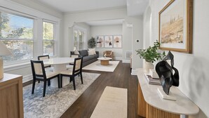 A modern living room with a dining area, featuring a sofa, chairs, a coffee table, and artwork on the walls.