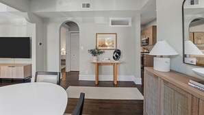 A modern living room with a flat-screen TV, a dining table, and a console table with a lamp.