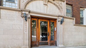 A building entrance with a wooden door, a number "1355-57" on the glass, and two wall-mounted lamps.
