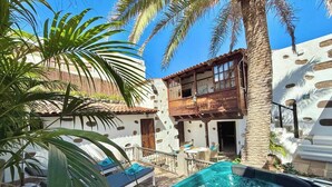 A pool area with lounge chairs, a wooden deck, and a white building with a balcony.