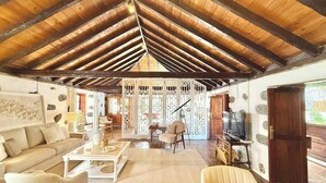 A spacious living room with a high wooden ceiling, a sofa, a coffee table, and a television.