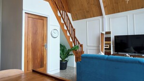 Ein Wohnzimmer mit einer Holztreppe, einem blauen Sofa, einem Flachbildfernseher und einem Blumentopf.