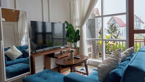 Ein Wohnzimmer mit großem Flachbildfernseher, einem blauen Sofa, einem Couchtisch und Blick durch große Fenster nach draußen.