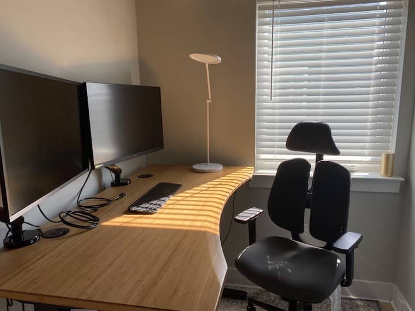 Et værelse med skrivebord, stol, fjernsyn, lampe og et vindue med persienner.