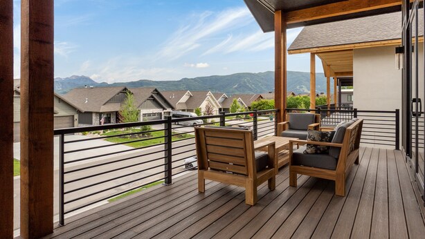 Una terraza de madera con una mesa y sillas, con vista a una calle y montañas.