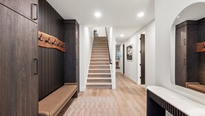 Un pasillo moderno con un banco de madera, un perchero y una escalera que lleva a otra habitación.