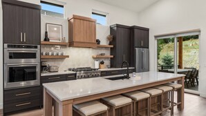 Una cocina moderna con armarios oscuros, una isla grande con taburetes y vistas al exterior a través de una puerta corrediza de vidrio.
