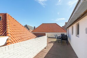 Una terrazza sul tetto con pavimento in legno, pareti in mattoni bianchi e tetti in tegole rosse.