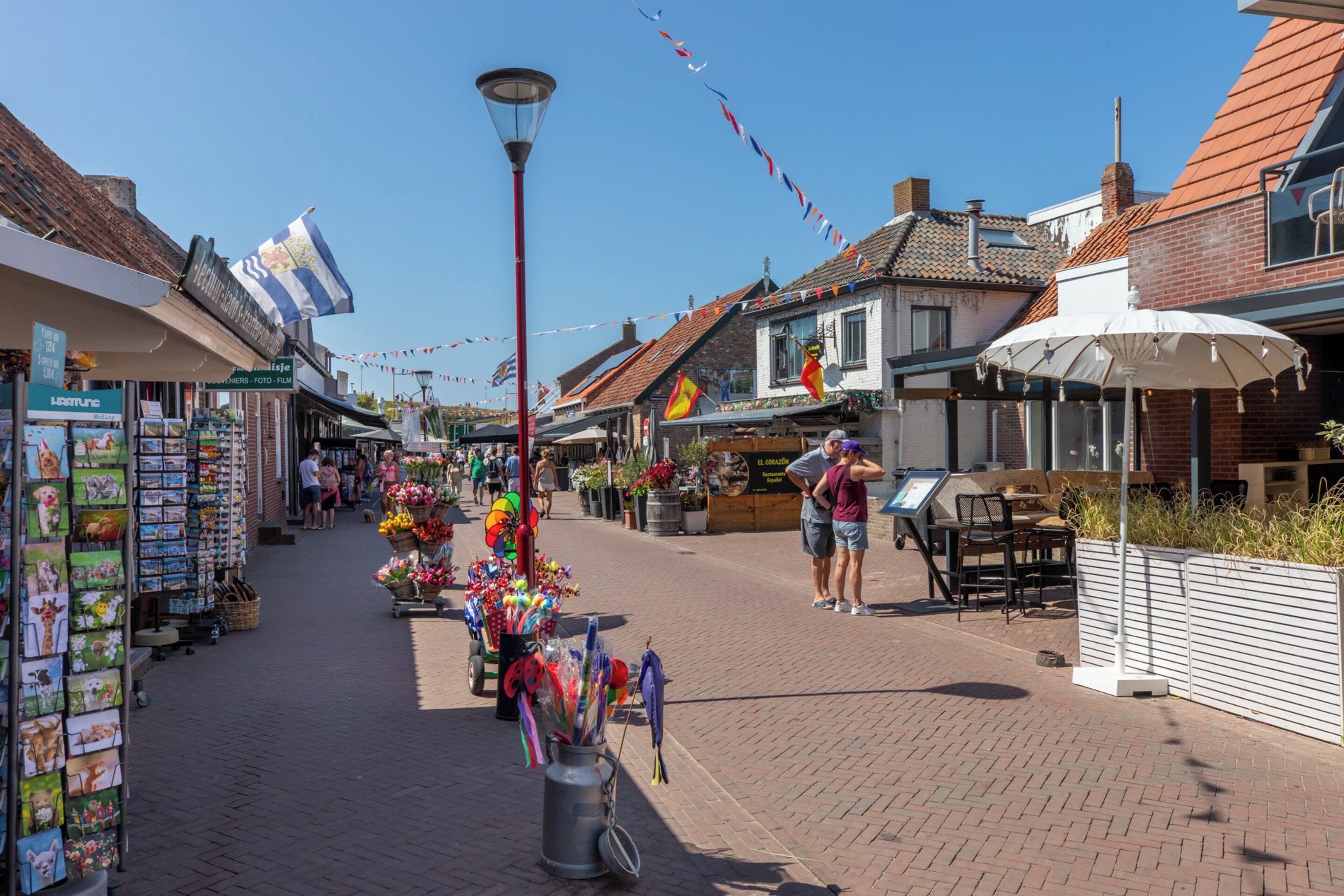 A street with shops, a street lamp, and a café with outdoor seating.