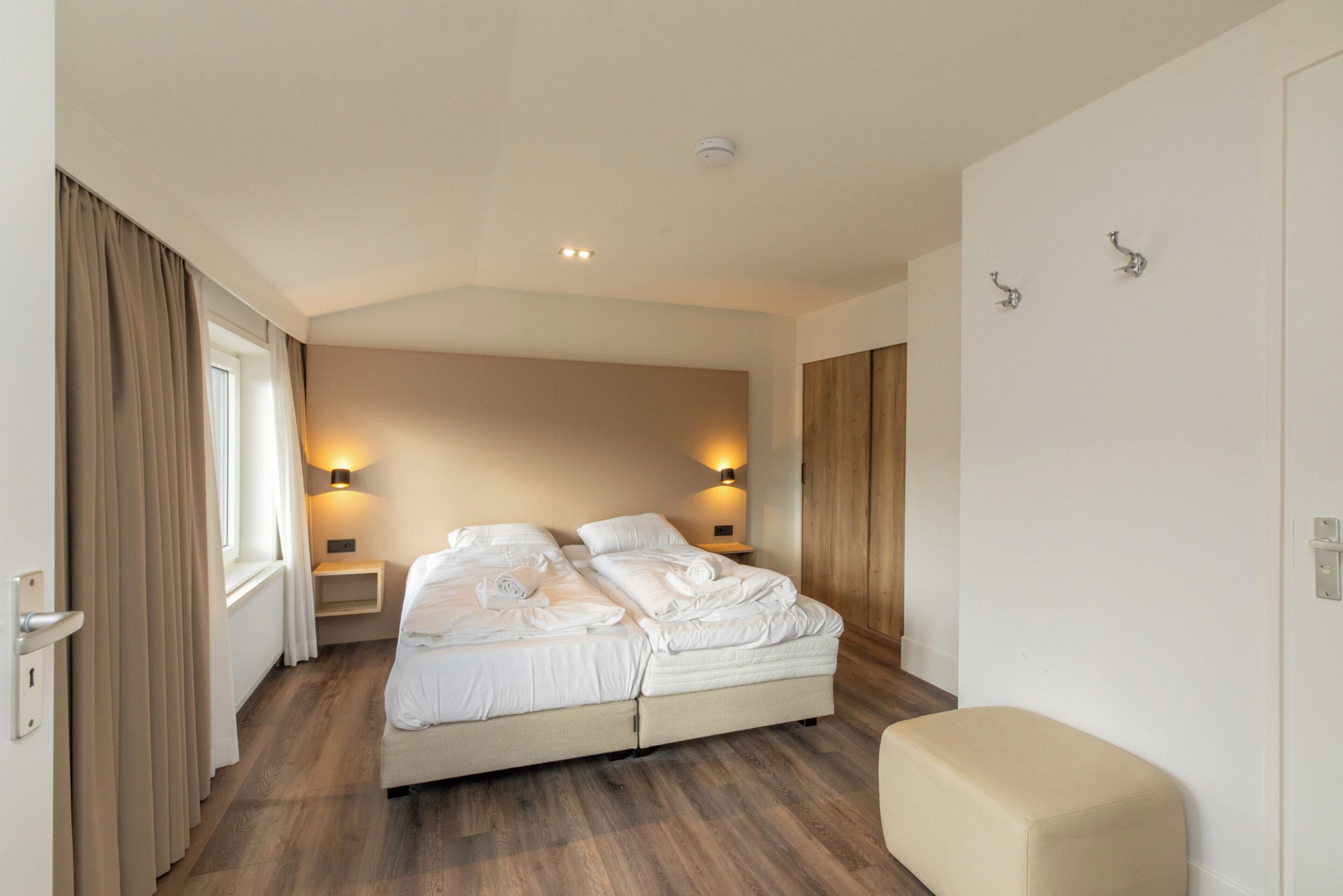Ein Hotelzimmer mit einem großen Bett, Nachttischen, einer Bank und einem Fenster mit Vorhängen.