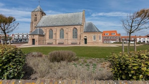 Een historisch kerkgebouw met een opvallende toren en rondboogvensters, omringd door een verzorgd gazon en volwassen bomen.