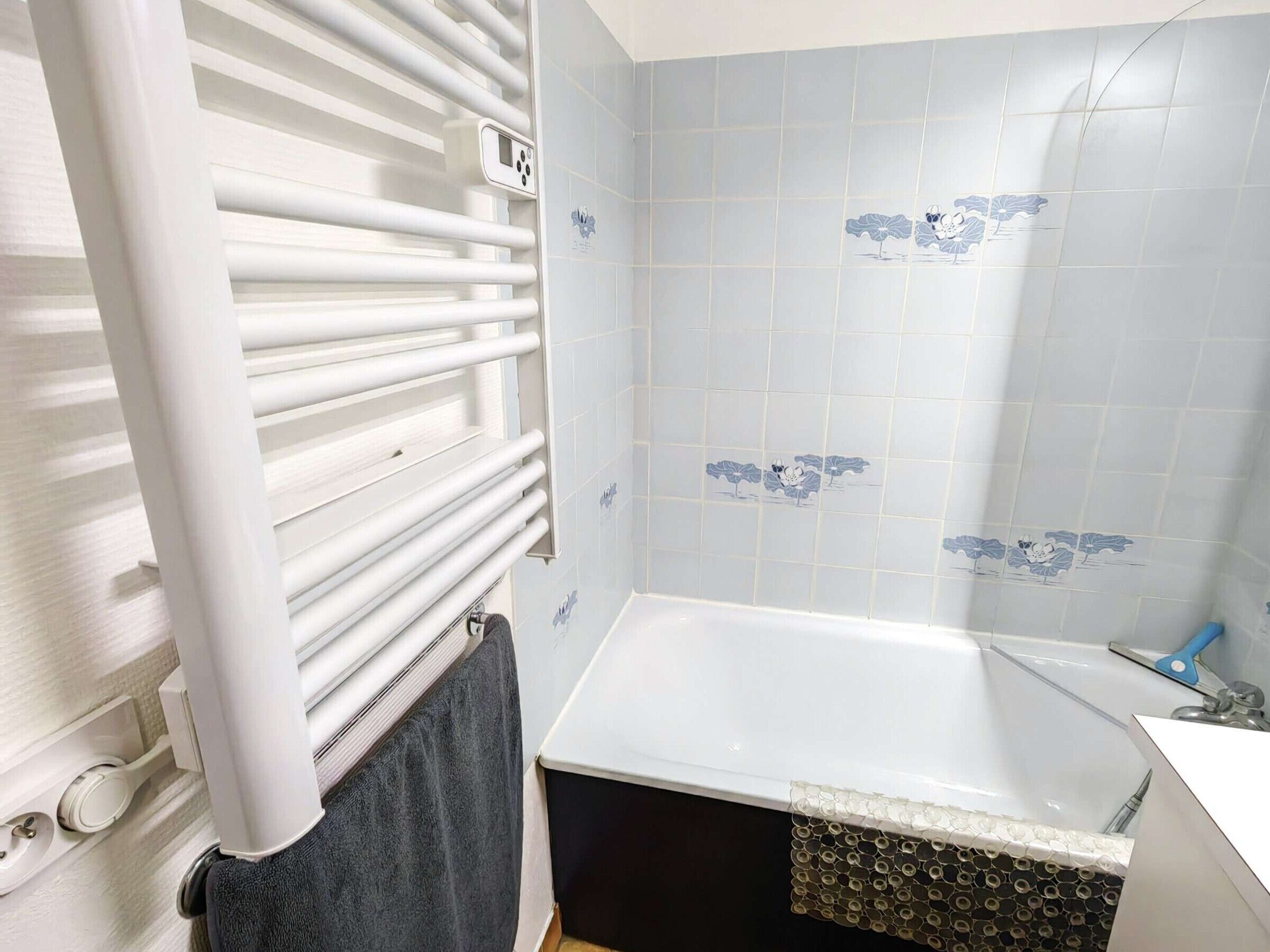 A bathroom with a bathtub, a white towel, and a shower with a blue handle.