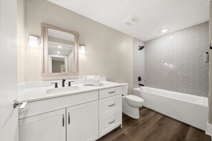 A modern bathroom with a white vanity, a large mirror, a toilet, and a bathtub.