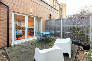 Une terrasse avec une table et des chaises, une clôture en bois et un bâtiment en briques.
