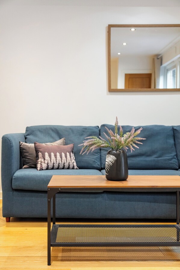 Un canapé bleu agrémenté de coussins décoratifs, une table basse en bois avec une plante, et un miroir accroché au mur.