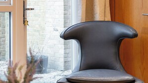 Ein modernes Interieur mit einem schwarzen Ledersessel, einem Holztisch und einem Topf mit einer Pflanze mit weißen Blättern.