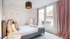 Ein modernes Schlafzimmer mit Bett, Nachttisch, Lampe und Blick ins Freie.