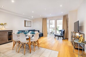 Un salon moderne comprenant un coin repas, un canapé, un téléviseur et un balcon agrémenté de rideaux.