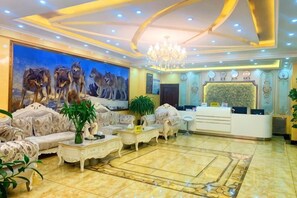 A spacious living room with a reception desk, plush seating, a large painting, and a chandelier.