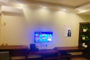 Zona de recepción con televisor de pantalla plana montado en la pared, mostrador de madera y estantería con plantas.