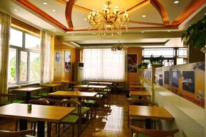 Un restaurante con varias mesas y sillas, un candelabro y amplias ventanas.