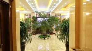 Un vestíbulo de hotel con piso de mármol, plantas en macetas y una recepción.