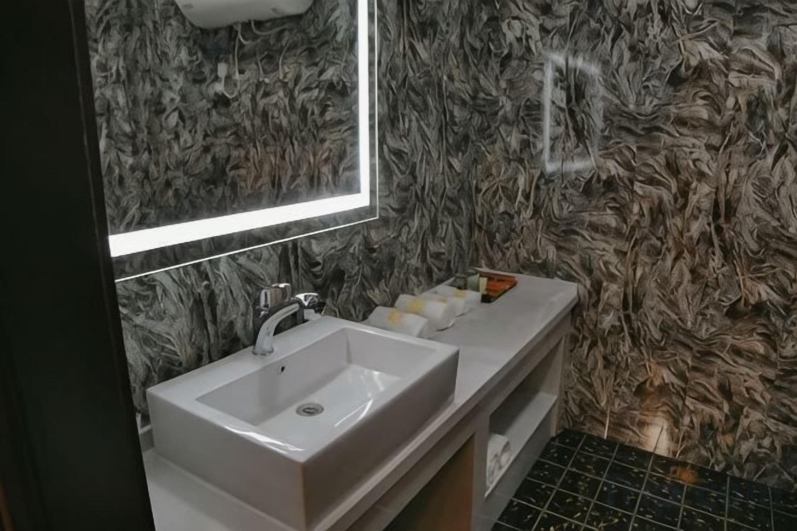 Ein Badezimmer mit einem weißen Waschbecken, einem Spiegel und einer wandartigen Marmorstruktur.