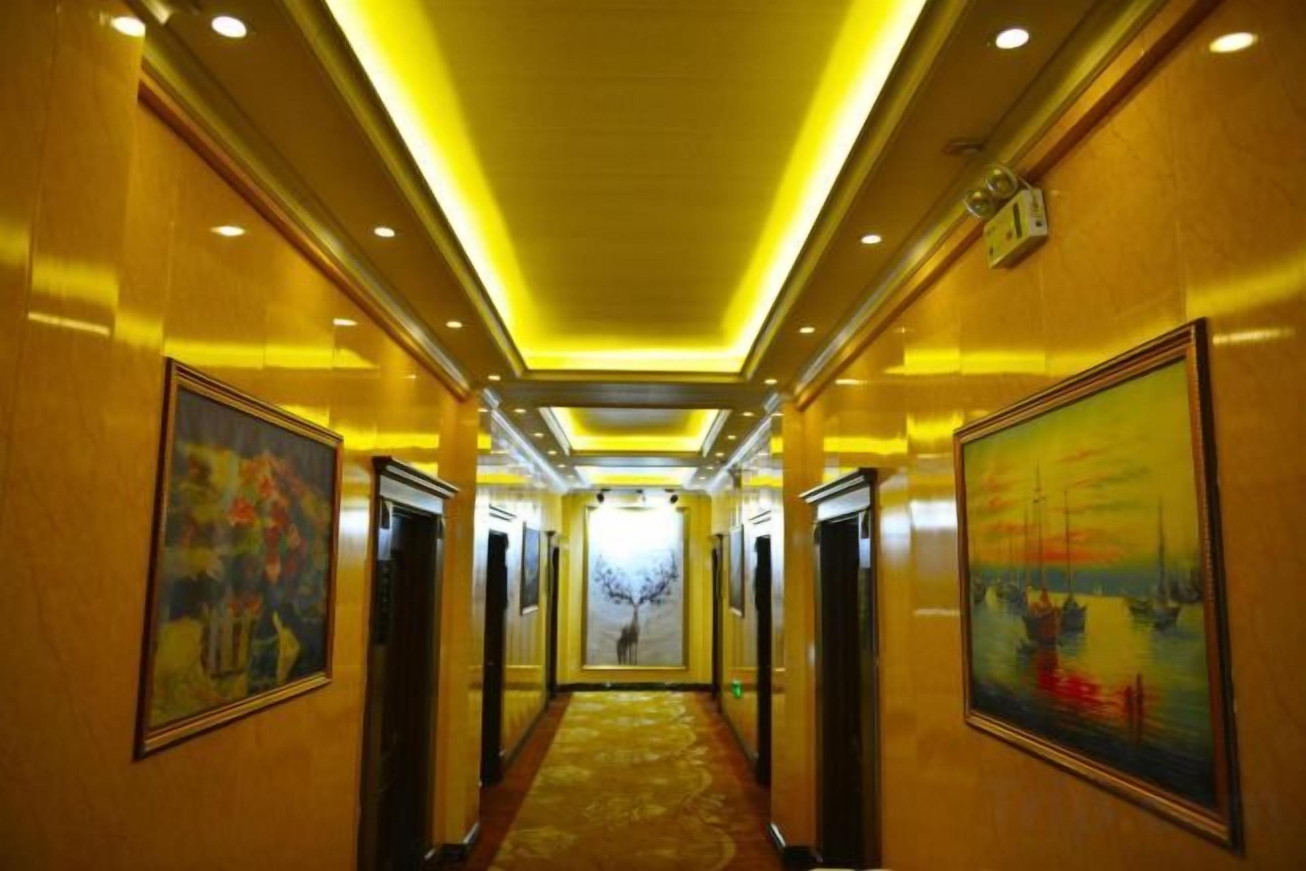 A hotel hallway with artwork on the walls, a carpeted floor, and a ceiling with recessed lighting.