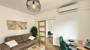 A modern living room with a brown sofa, a white coffee table, and a dining area with teal chairs and a wooden table. - 06CP - Beautiful T2 super equipped with terrace (Villeneuve-Loubet)